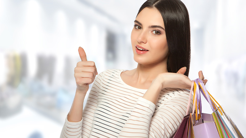 A woman with shopping bags, happy with her discounted purchase.